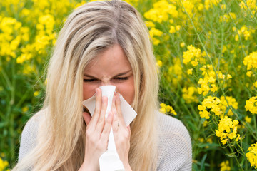 Young woman suffers from allergy in a rape field and has to sneeze