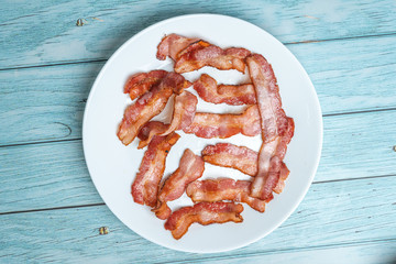 Cooked fired bacon rashers white dish and blue wooden background, Morning Breakfast Concept, View from Top, Flat Lay 