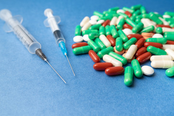 many multi-colored medical antiviral pills with syringe on blue background close-up