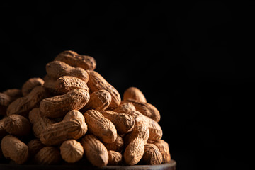 Close up of raw groundnuts kept in a wooden bowl on a black background. 
