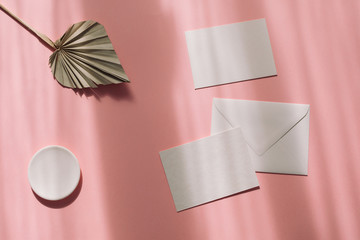 White envelope, paper sheets decorated with palm leaf on pastel pink shadow background. Wedding...