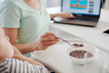 Obraz premium Close up of mother feeding child with spoon and working on computer