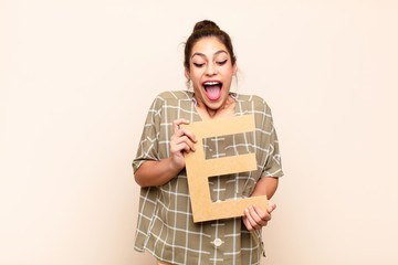 young pretty woman surprised, shocked, amazed, holding the letter E of the alphabet to form a word...