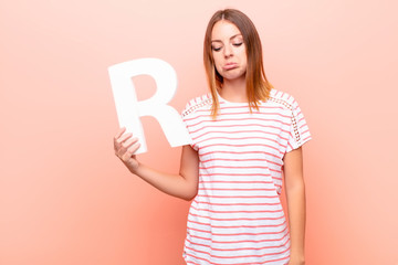 young pretty red head woman sad, depressed, unhappy, holding the letter R of the alphabet to form a...
