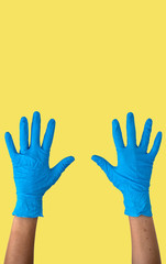 Human rising hands wearing blue disposable latex glove, rubber glove for professional medical safety and hygiene protection from Coronavirus disease COVID-19 and medical surgery on yellow background