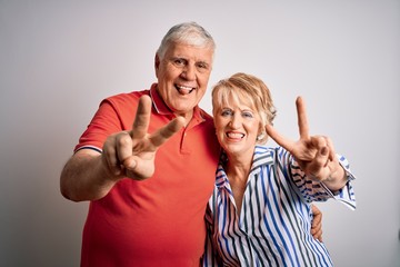 Senior beautiful couple standing together over isolated white background smiling with tongue out showing fingers of both hands doing victory sign. Number two.