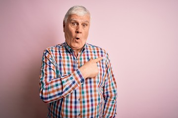 Senior handsome hoary man wearing casual colorful shirt over isolated pink background Surprised pointing with finger to the side, open mouth amazed expression.