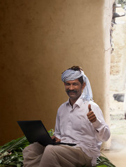 Rural farmer showing thumb up while working on laptop
