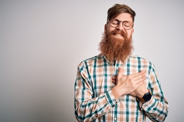 Handsome Irish redhead man with beard wearing glasses and hipster shirt smiling with hands on chest with closed eyes and grateful gesture on face. Health concept.