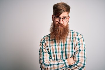 Handsome Irish redhead man with beard wearing glasses and hipster shirt skeptic and nervous, disapproving expression on face with crossed arms. Negative person.
