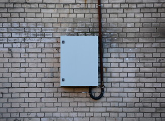 Closed metal electrical panel on a white brick wall with a cable running from it