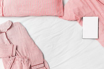 Pink pajamas,  blanket and pillow with striped on white sheet  in bed with copy space. Night suit clothes for sleeping and closed book. Copy space. Top view. Flat lay.