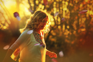 Romantisch: Blonde Frau bei Sonnenuntergang mit Blütenblättern
