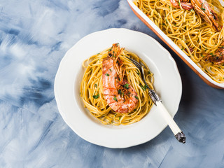Linguine pasta with tiger prawn sauce in white dish over blue and white background. Seafood dish