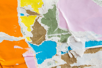 Torn and crumpled pieces of paper placards on urban billboard. Old colorful ripped and peeling...