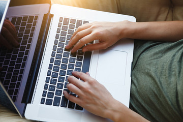 female hands typing on laptop, young woman sitting at home and working online or watching video at the morning sunlight
