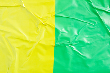 Yellow and green crumpled glossy paper posters glued on billboard texture background.