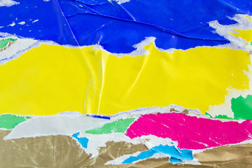 Blue and yellow torn, crumpled and shabby pieces of paper placards on urban billboard. Bright colorful ripped and peeling posters with scratches texture background.