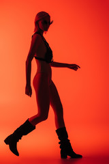 Fototapeta na wymiar fashionable futuristic girl posing in bodysuit and fire-shaped sunglasses on red