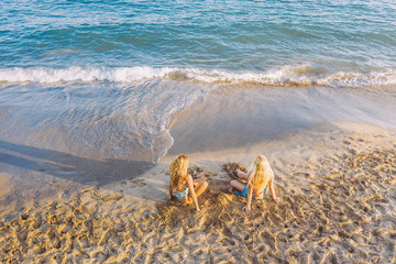 Fototapeta na wymiar two blond women sitting on the shore of the beach