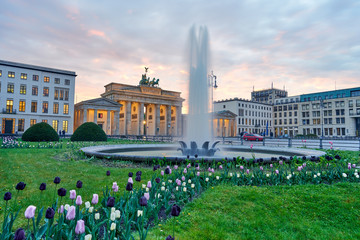 Fototapety  Wonderful panoramic view over colorful tulips in green grass past a fountain on the Berlin Brandenburg Gate in the sunset with beautiful clouds. Spring time in Germany - paris square in Berlin city