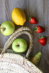 Straw bag with apples, bananas, pear, lemon and strawberries. Top view.
