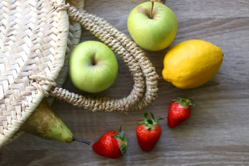 Fototapeta na wymiar Straw bag with apples, bananas, pear, lemon and strawberries. Top view.