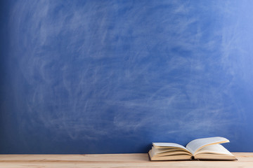 Education and reading concept - group of books on the wooden table, blue blackboard background. Teachers desk