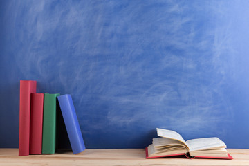 Education and reading concept - group of books on the wooden table, blue blackboard background. Teachers desk