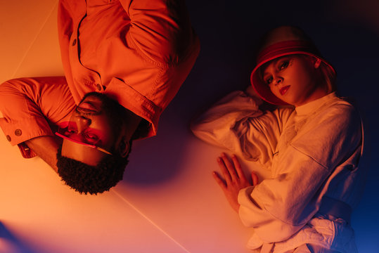 top view of interracial couple in futuristic clothes lying in orange light