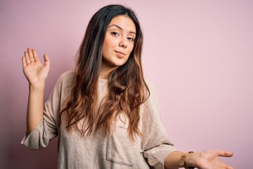 Young beautiful brunette woman wearing casual sweater standing over pink background clueless and...