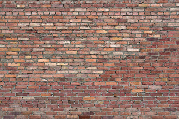 Old brick wall of red blocks with crumbling texture.
