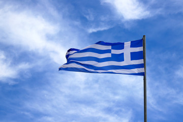 The national state flag of Greece with white and blue stripes and a cross flies against a blue cloudy sky, beautiful view of the Greek flag