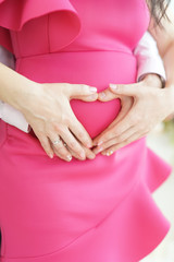 Heart-shaped hands on the belly of a pregnant woman in a pink dress