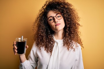 Young beautiful woman with curly hair and piercing wearing glasses drinking glass of coffee with a...