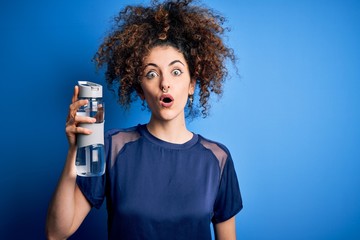 Young beautiful sporty woman with curly hair and piercing doing sport holding bottle of water scared in shock with a surprise face, afraid and excited with fear expression