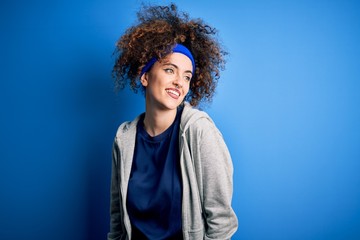 Fototapeta na wymiar Young beautiful sportswoman with curly hair and piercing standing wearing sportswear looking away to side with smile on face, natural expression. Laughing confident.