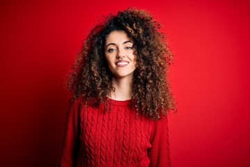 Young beautiful woman with curly hair and piercing wearing casual red sweater with a happy and cool smile on face. Lucky person.