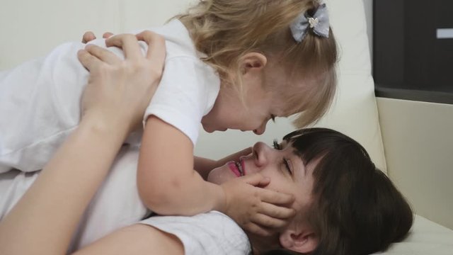 Happy family. A young mother with a blonde daughter play on the couch at home, a girl holds a laughing child in her arms.