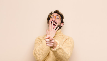 young cool man laughing at you, pointing to camera and making fun of or mocking you against flat...