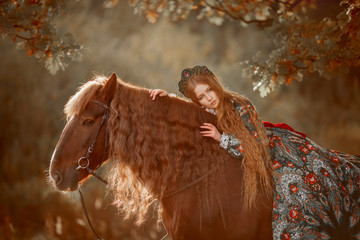 Beautiful long-haired blonde young woman in national russian style with red Vladimir draft horse in autumn forest