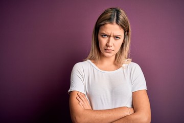 Young beautiful blonde woman wearing casual white t-shirt over purple isolated background skeptic and nervous, disapproving expression on face with crossed arms. Negative person.