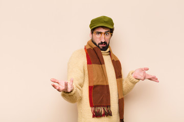 young cool bearded man shrugging with a dumb, crazy, confused, puzzled expression, feeling annoyed...