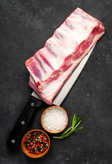 raw pork ribs with spices and rosemary on a knife on a stone background