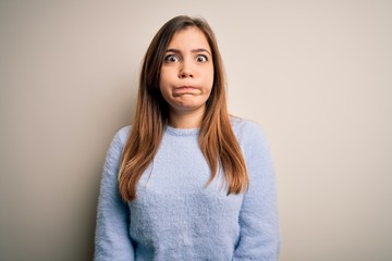 Fototapeta premium Beautiful young woman wearing casual winter sweater standing over isolated background puffing cheeks with funny face. Mouth inflated with air, crazy expression.