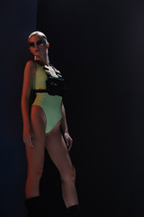 attractive stylish girl in futuristic leotard and fire-shaped sunglasses posing on dark
