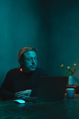 Man with eyeglasses working at home behind laptop in the evening.