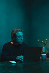 Man with eyeglasses working at home behind laptop in the evening.