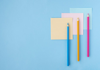 Flat lay with colored pencils and pieces of paper on blue background. Top view, copy space. Concept back to school, education, office