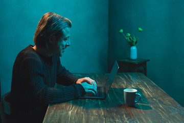 Naklejka premium Man behind laptop working at home in the evening. Side view.